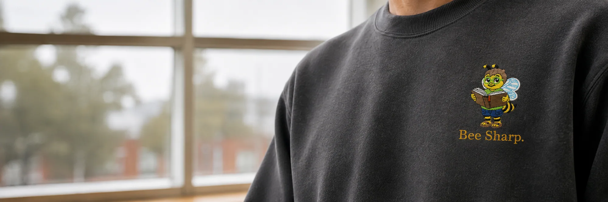 A person in a charcoal Bee Sharp crewneck sweatshirt, from the chest down.
