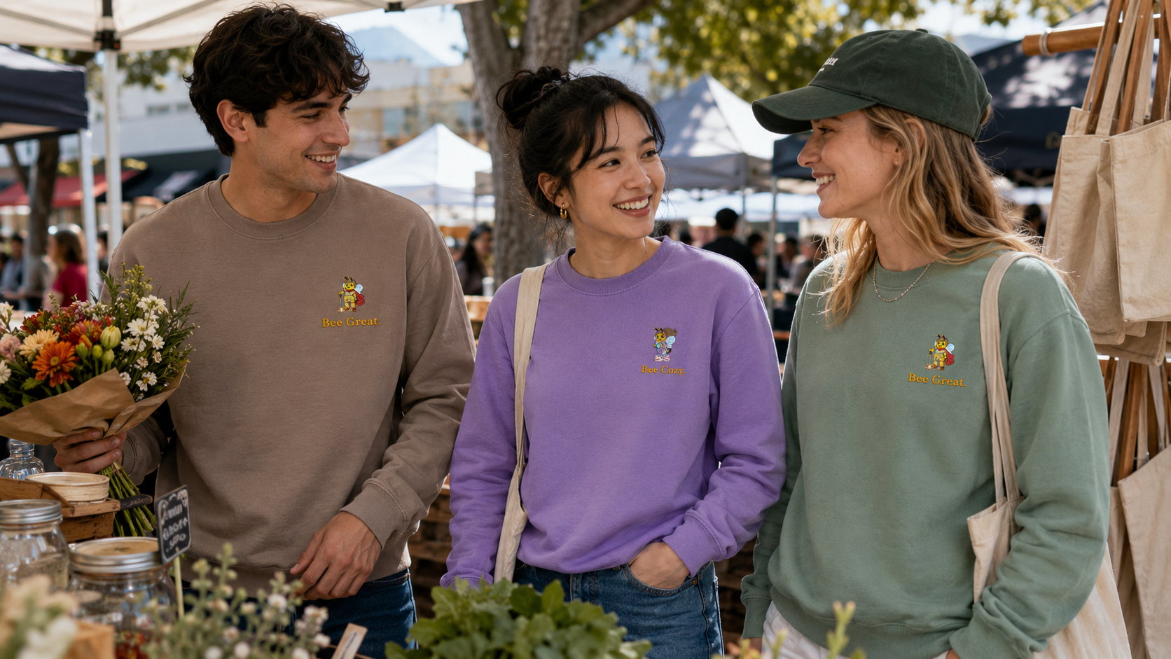 Three friends at an outdoor market wearing embroidered Bee Cheever sweatshirts.